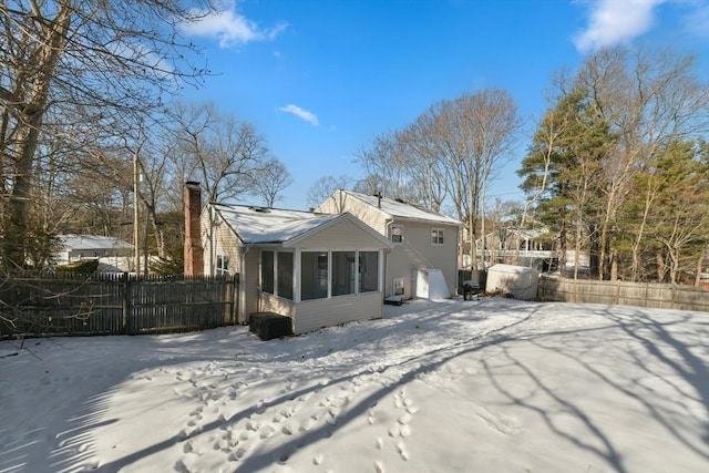 snow covered rear of property featuring a sunroom