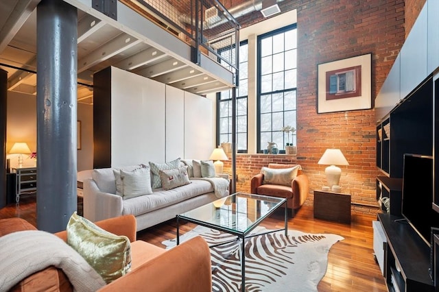 living room with a towering ceiling, hardwood / wood-style floors, brick wall, and ornate columns