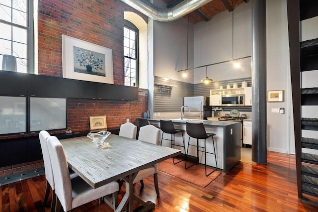 dining area with a towering ceiling, wood finished floors, and brick wall
