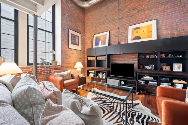 living room featuring a towering ceiling, brick wall, and wood finished floors