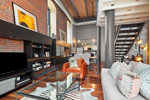 living area with a high ceiling, stairway, wood finished floors, and brick wall