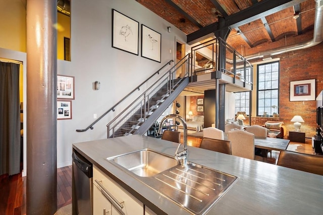 kitchen featuring a high ceiling, dark wood-style flooring, dishwasher, brick wall, and a sink