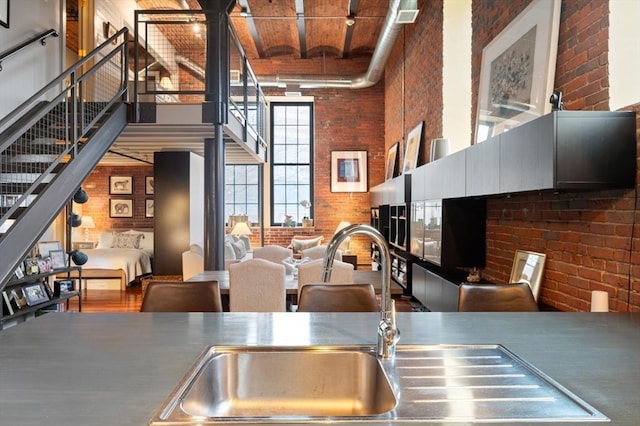 kitchen with a towering ceiling, brick wall, a sink, stainless steel counters, and open floor plan
