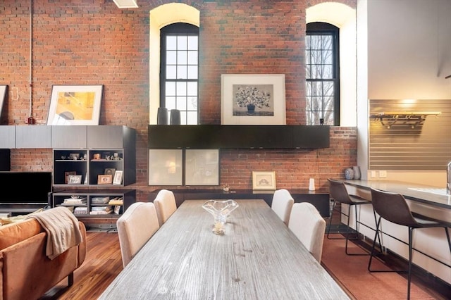 dining room featuring brick wall, wood finished floors, healthy amount of natural light, and a high ceiling