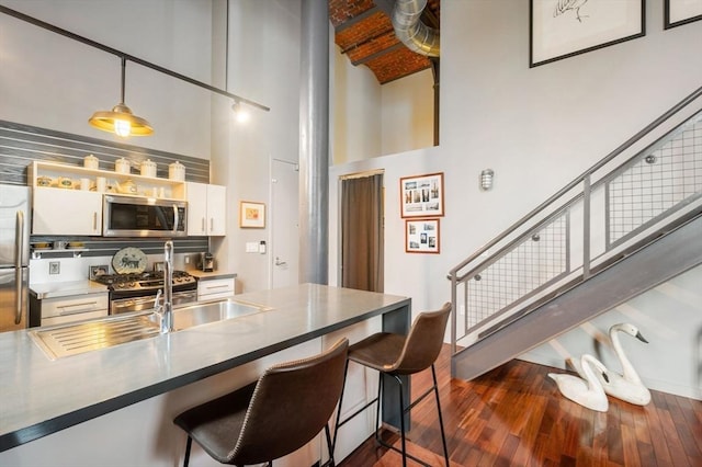 kitchen featuring stainless steel appliances, a towering ceiling, a kitchen breakfast bar, dark wood-style floors, and white cabinetry