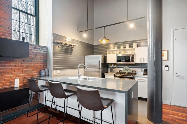 kitchen featuring stainless steel appliances, a sink, white cabinets, a kitchen bar, and a peninsula