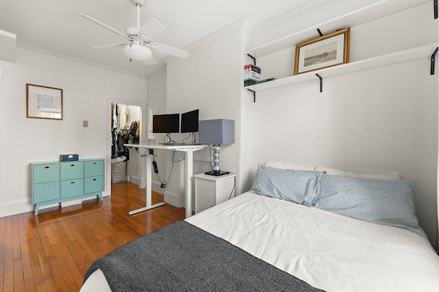 bedroom with a walk in closet, ornamental molding, hardwood / wood-style flooring, a closet, and a ceiling fan