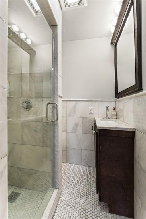 bathroom with visible vents, a stall shower, tile walls, tile patterned flooring, and vanity