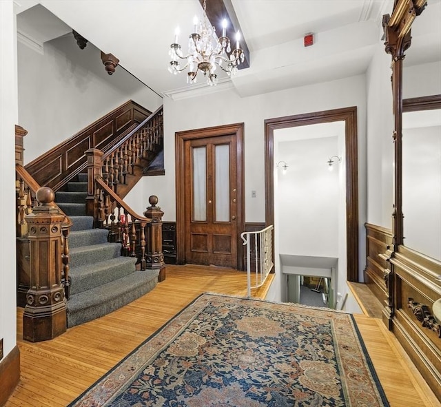 entryway with wood finished floors, an inviting chandelier, ornamental molding, stairs, and wainscoting