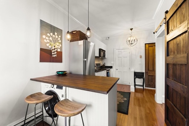 kitchen featuring butcher block counters, a barn door, ornamental molding, appliances with stainless steel finishes, and wood finished floors