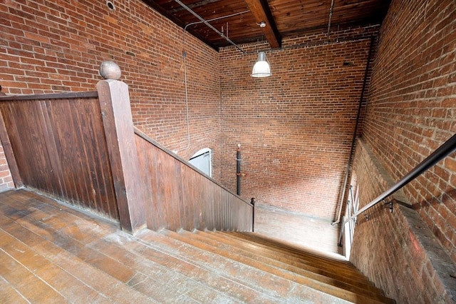 stairway featuring brick wall, a high ceiling, wood finished floors, and beamed ceiling