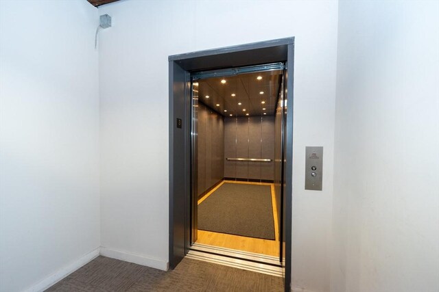 room details featuring elevator, baseboards, and carpet flooring