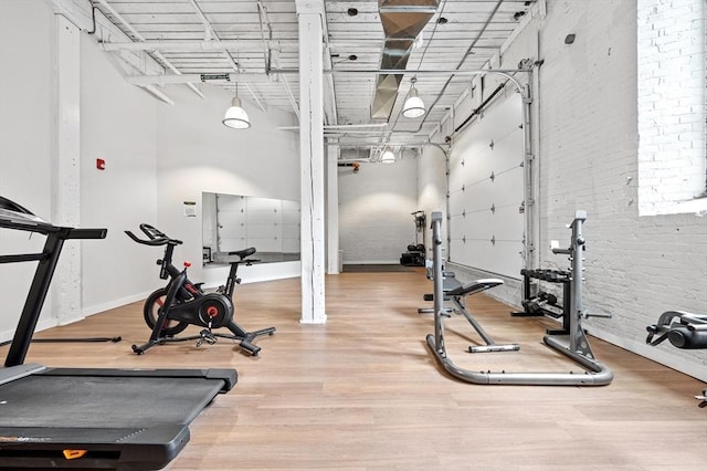 exercise room with a garage, brick wall, wood finished floors, and baseboards