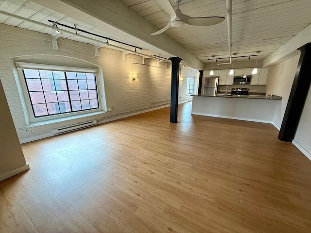 unfurnished living room with rail lighting, baseboard heating, a sink, brick wall, and light wood-type flooring