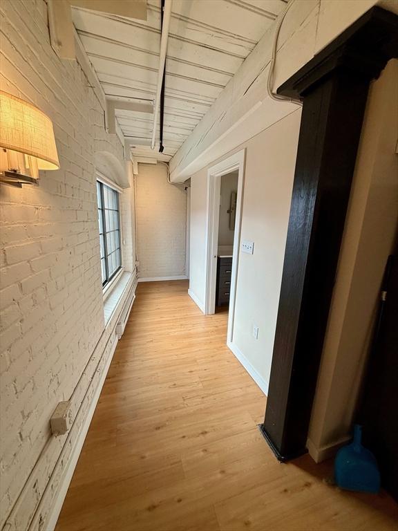 hallway with beam ceiling, brick wall, baseboards, and light wood finished floors