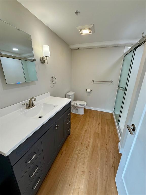 full bathroom featuring toilet, wood finished floors, vanity, baseboards, and a shower stall