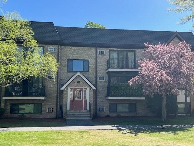 view of property featuring a balcony, a front yard, and entry steps