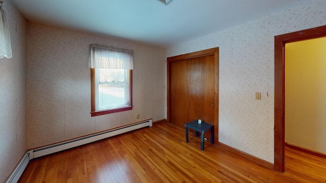 unfurnished bedroom with light wood-type flooring, a closet, and a baseboard heating unit