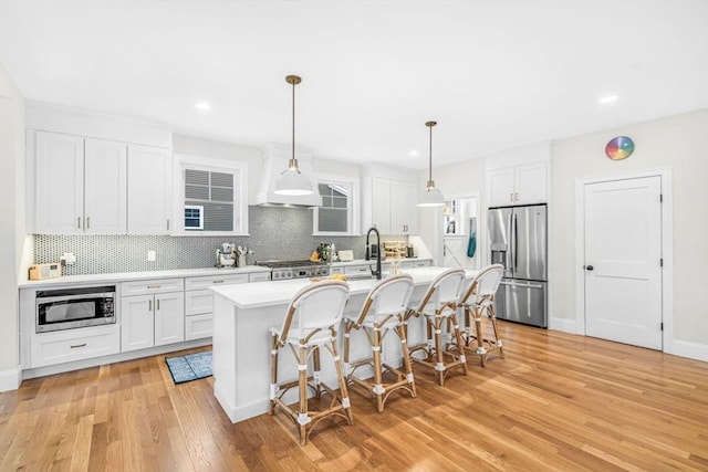 kitchen featuring appliances with stainless steel finishes, light countertops, a center island with sink, and white cabinetry