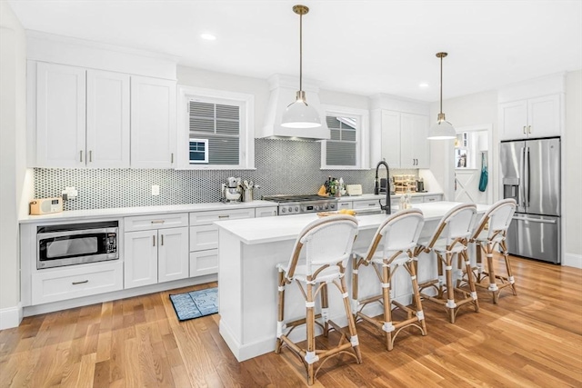 kitchen with a center island with sink, a breakfast bar area, stainless steel appliances, light countertops, and light wood-type flooring