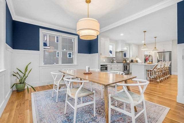 dining room with a wainscoted wall, light wood-style flooring, and ornamental molding