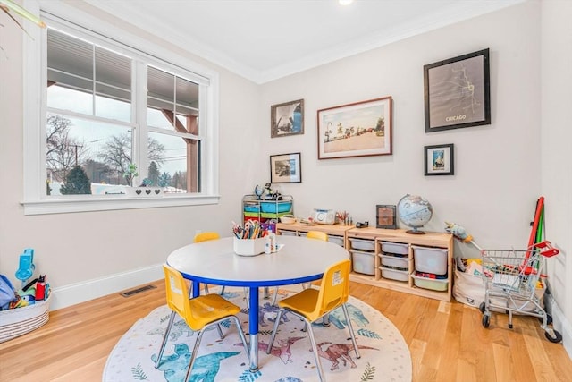 recreation room with baseboards, wood finished floors, visible vents, and crown molding