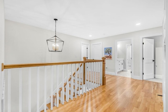 hall with light wood-style flooring, recessed lighting, an upstairs landing, baseboards, and an inviting chandelier