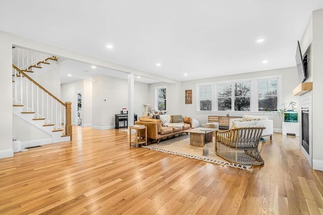 living room featuring a healthy amount of sunlight, light wood-style flooring, stairway, and a glass covered fireplace