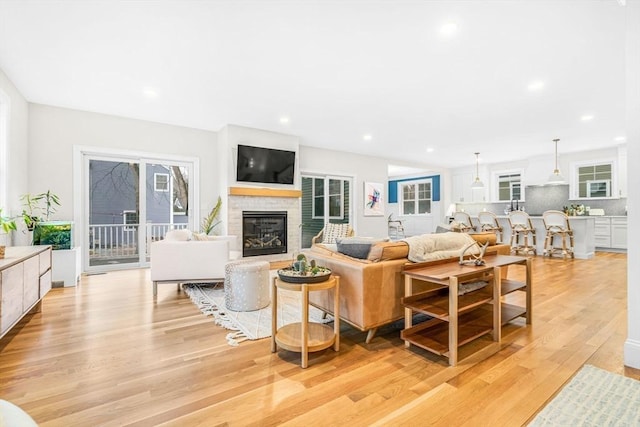 living area featuring light wood finished floors, a glass covered fireplace, and recessed lighting