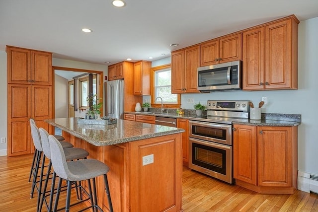kitchen with a center island, brown cabinets, a breakfast bar area, light wood-style flooring, and appliances with stainless steel finishes