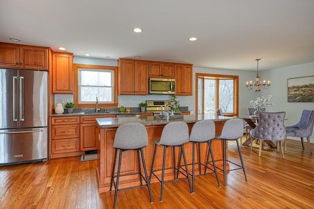 kitchen with brown cabinetry, stainless steel appliances, light wood-style flooring, a kitchen bar, and a kitchen island