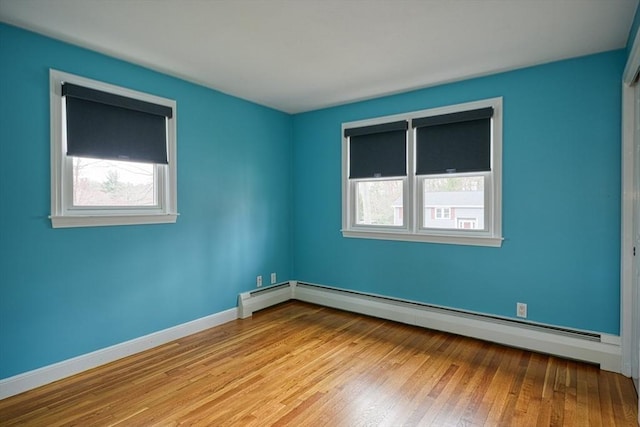 empty room featuring wood-type flooring, baseboards, a baseboard radiator, and a healthy amount of sunlight