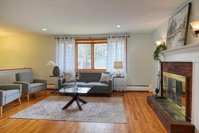 living area with a baseboard radiator, hardwood / wood-style floors, a brick fireplace, and a baseboard heating unit