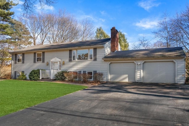 raised ranch with a garage, a chimney, a front yard, and aphalt driveway