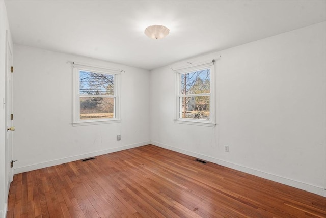 empty room featuring hardwood / wood-style flooring, baseboards, and visible vents