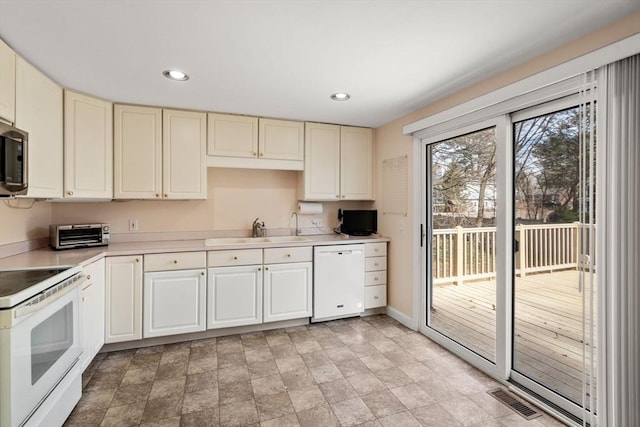 kitchen with visible vents, cream cabinetry, a sink, white appliances, and light countertops