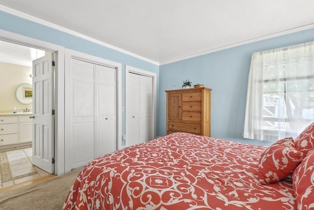 bedroom featuring two closets, light carpet, ornamental molding, and connected bathroom