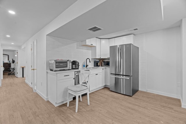 kitchen featuring visible vents, backsplash, light wood-style flooring, appliances with stainless steel finishes, and a sink