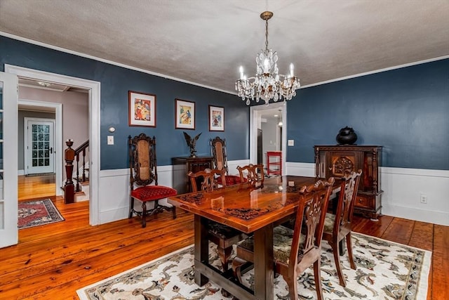 dining area featuring a wainscoted wall, stairway, an inviting chandelier, ornamental molding, and hardwood / wood-style floors