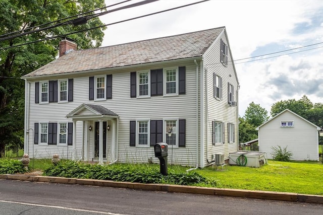 colonial home featuring central AC unit, a chimney, a front yard, and a shingled roof