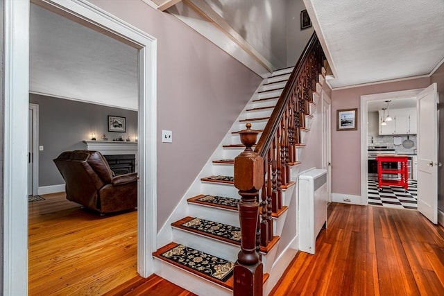 stairs featuring baseboards, a fireplace, ornamental molding, and hardwood / wood-style floors