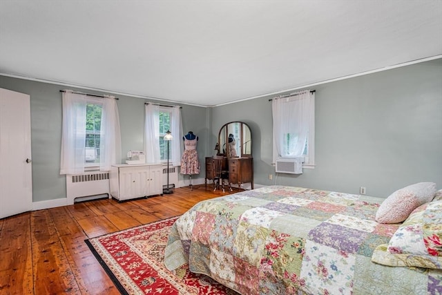 bedroom featuring baseboards, hardwood / wood-style flooring, radiator heating unit, ornamental molding, and cooling unit