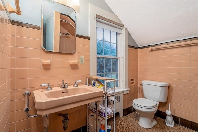 bathroom with tile walls, radiator heating unit, toilet, vaulted ceiling, and tile patterned flooring