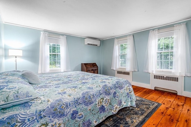 bedroom with radiator, crown molding, a wall unit AC, and wood finished floors