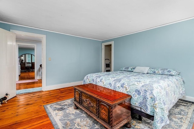 bedroom with arched walkways, crown molding, baseboards, and wood finished floors