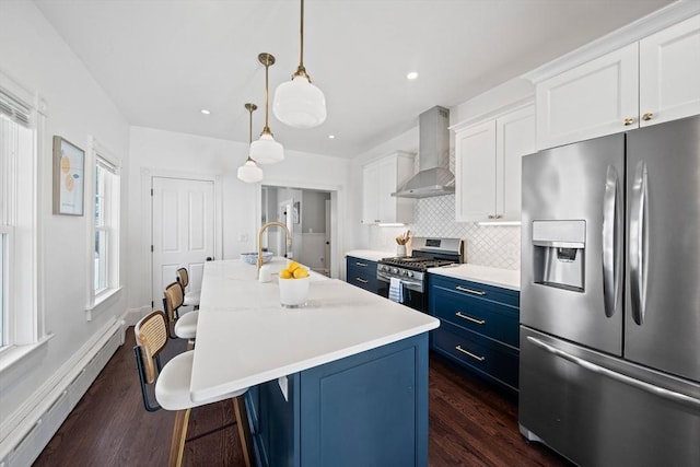 kitchen with a baseboard radiator, appliances with stainless steel finishes, blue cabinets, wall chimney range hood, and a sink