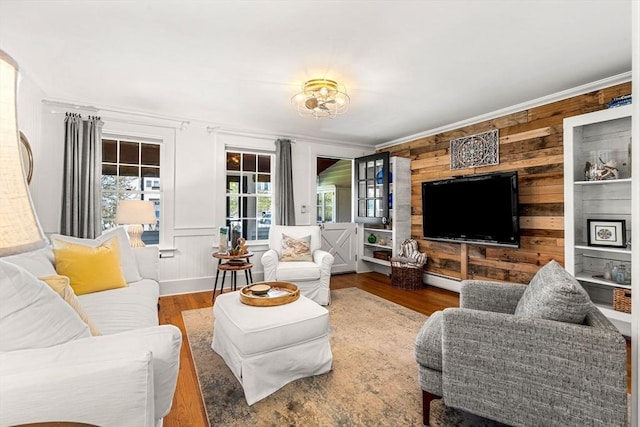 living room featuring crown molding, wooden walls, a baseboard heating unit, and wood finished floors