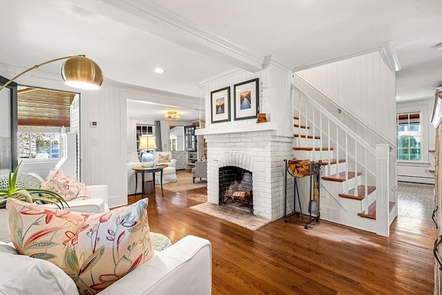living room with crown molding, a brick fireplace, stairs, and wood finished floors