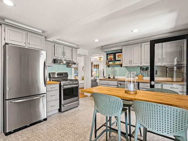 kitchen with appliances with stainless steel finishes, a sink, recessed lighting, under cabinet range hood, and butcher block counters