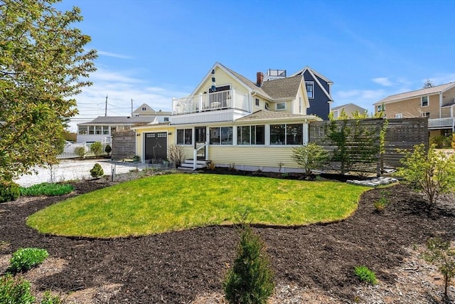rear view of house featuring an attached garage, a lawn, fence, and a balcony